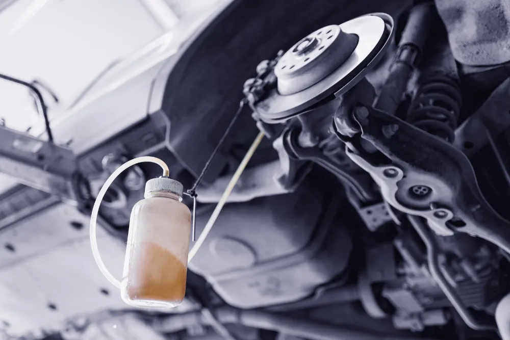Brake fluid flush, auto repair in New Braunfels, TX by Clark’s Auto Service. Image of brake fluid being bled from a vehicle’s braking system with a collection bottle attached under a lift. Highlighting hydraulic brake performance, responsive stopping power, and driver safety.