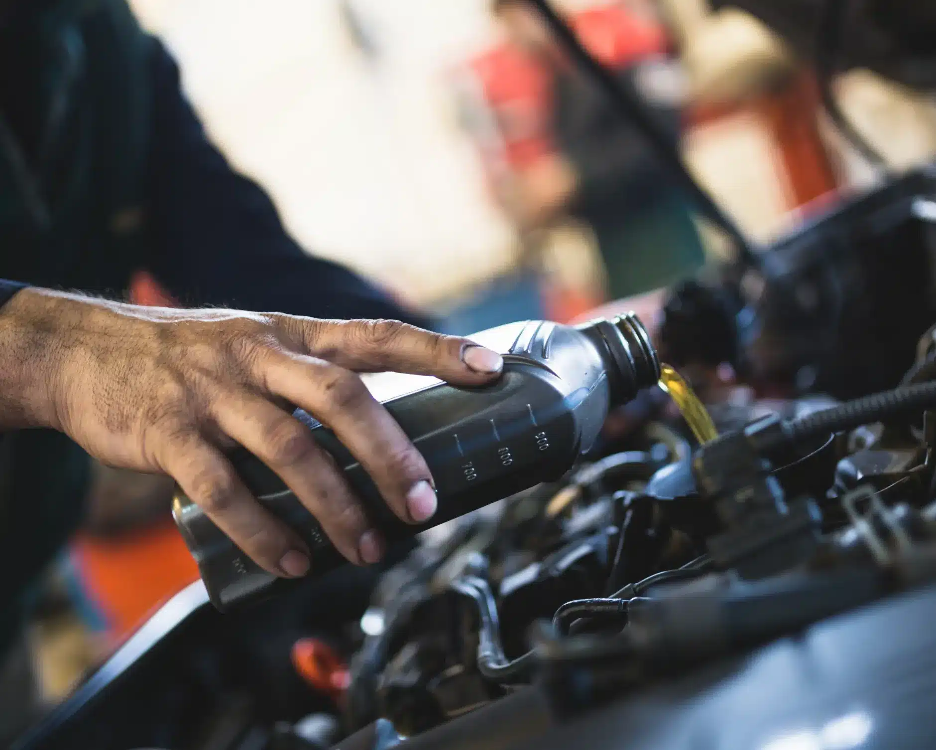 Careers, auto repair in New Braunfels, TX by Clark's Auto Service. A person’s hand pours motor oil from a gray bottle into a car engine, suggesting routine vehicle maintenance in a workshop setting.