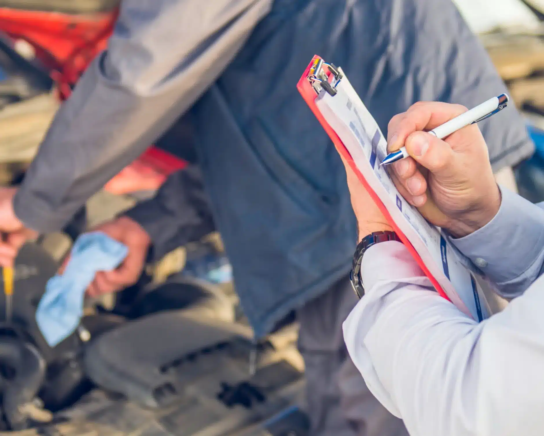 ADAS services in New Braunfels, TX by Clark's Auto Service. A person holding a clipboard and pen checks off a list while another person works on a car engine in the background, suggesting a vehicle inspection or maintenance process.