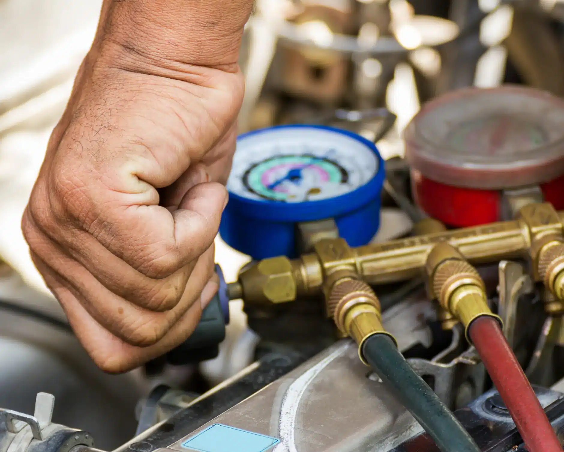 Auto a/c & heater repair in New Braunfels, TX by Clark's Auto ServiceA close-up of a person’s hand adjusting gauges on a manifold set, commonly used for checking and servicing car air conditioning systems, with colored hoses attached to the equipment.