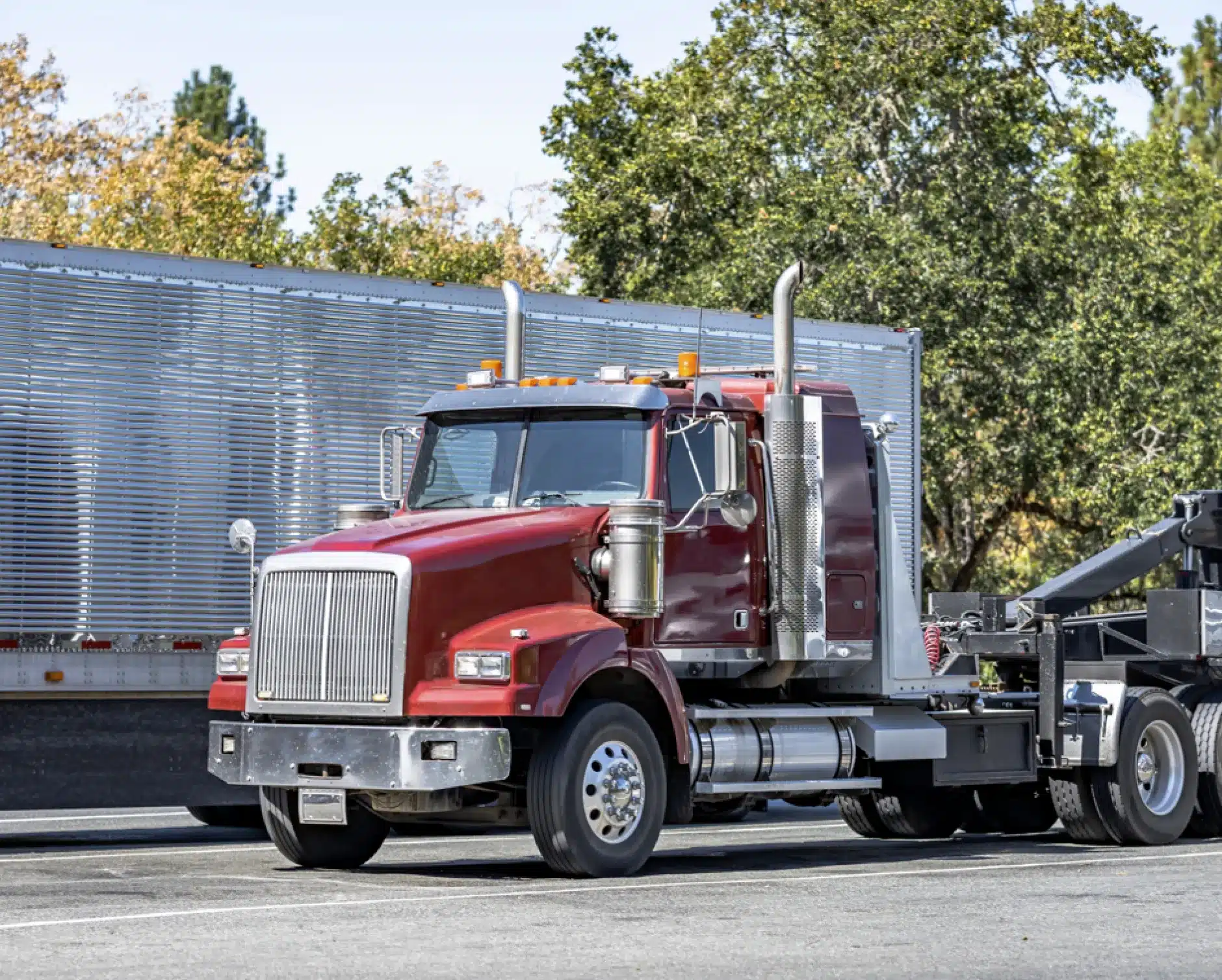 Fleet maintenance, auto repair in New Braunfels, TX by Clark's Auto Service. A red semi-truck cab is parked on a road next to a large silver trailer, with trees and a clear sky in the background.