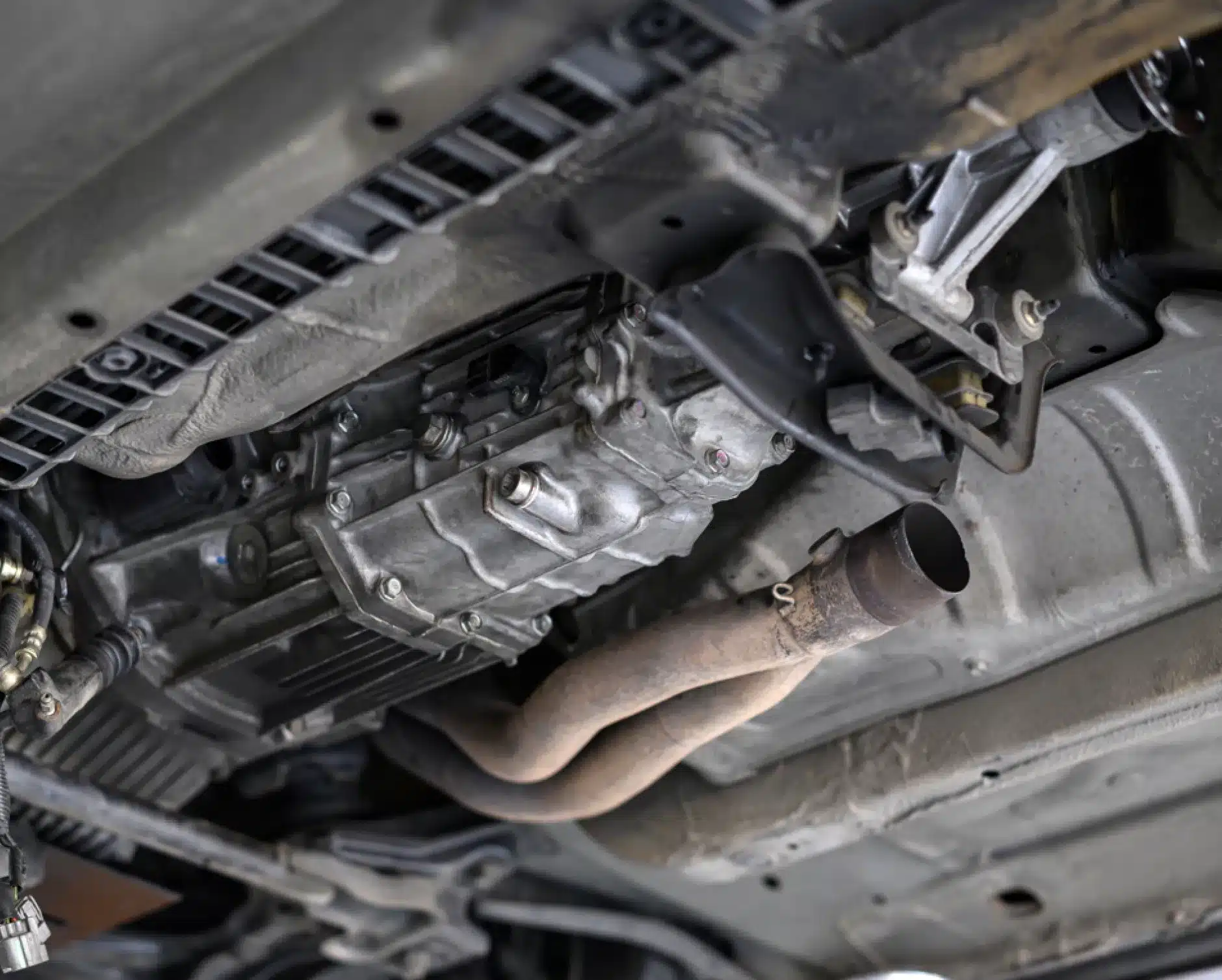 Transmission repair, auto repair in New Braunfels, TX by Clark's Auto Service. View of the underside of a vehicle showing the exhaust pipe, transmission, and various metal components and parts of the cars undercarriage.