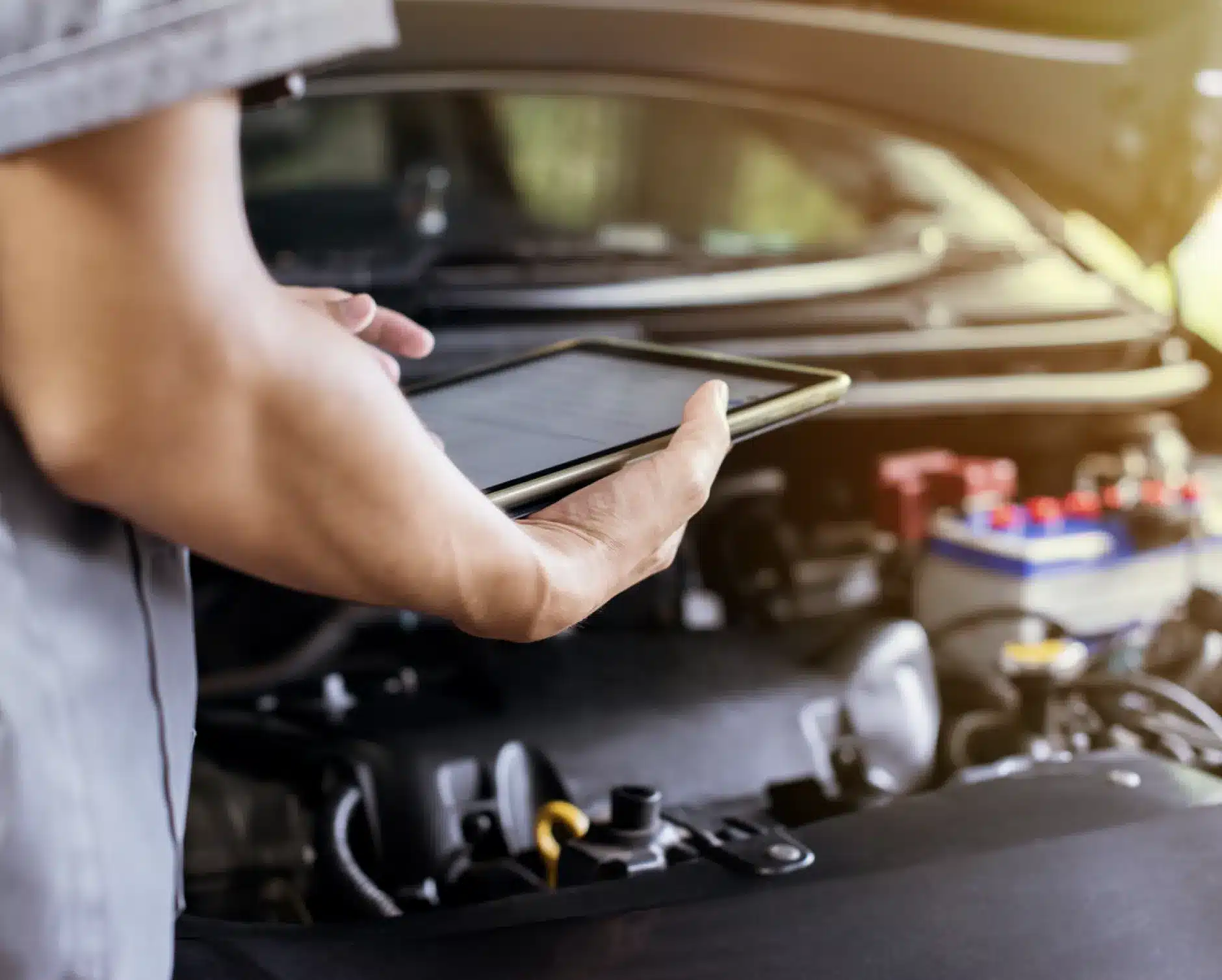 Vehicle inspections, auto repair in New Braunfels, TX by Clark's Auto Service. A person holding a tablet stands in front of an open car hood, using the device to inspect or diagnose the vehicle’s engine. The scene suggests a modern approach to car maintenance or repair.