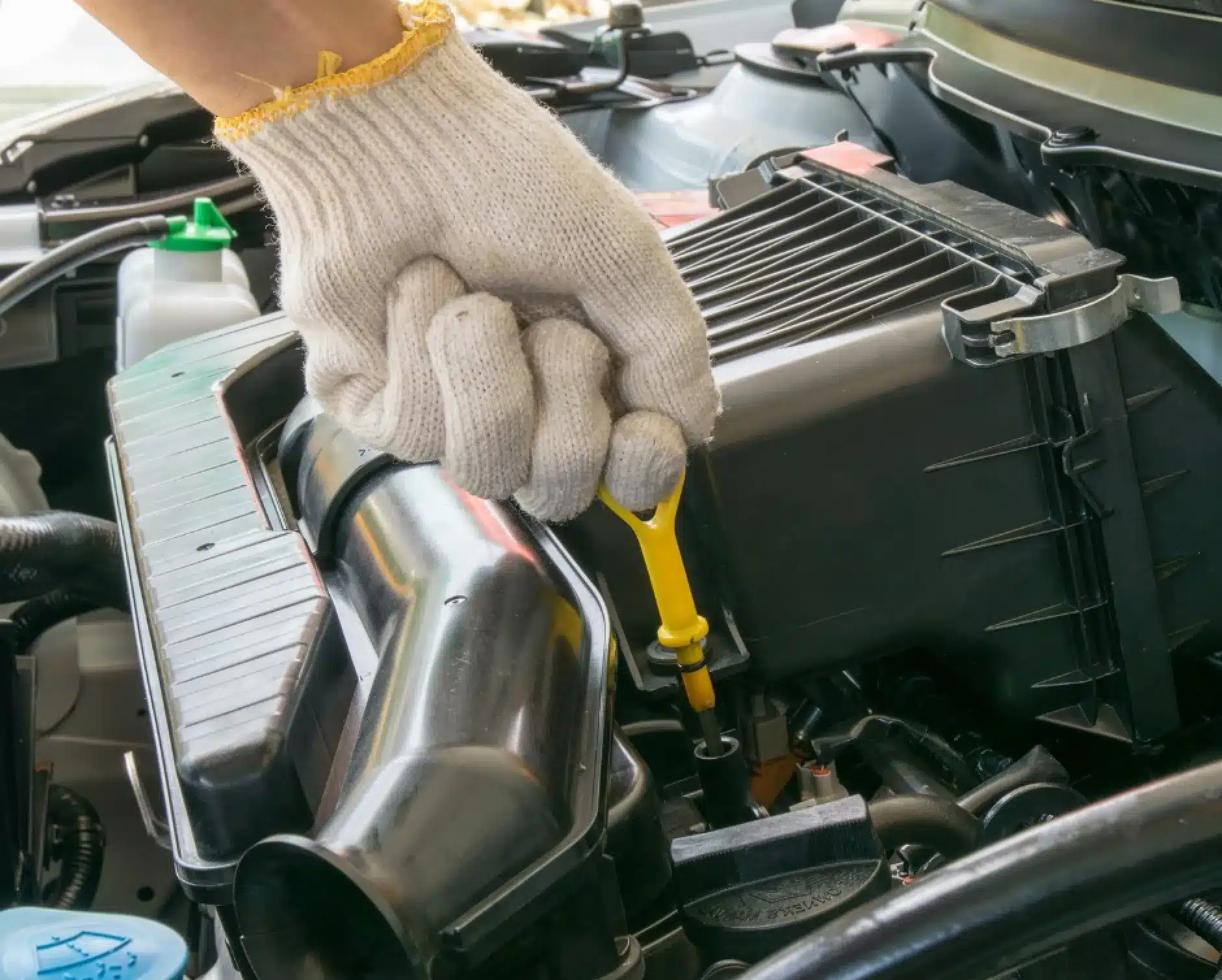 Vehicles we service, auto repair in New Braunfels, TX by Clark's Auto Service. A hand wearing a white glove with a yellow trim is pulling out the yellow oil dipstick from a car engine compartment for an oil check.