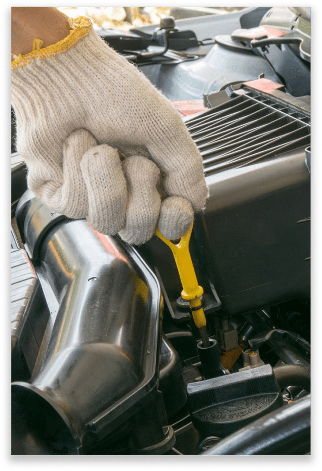 A person wearing a white glove is pulling out the yellow dipstick from a car engine to check the oil level.