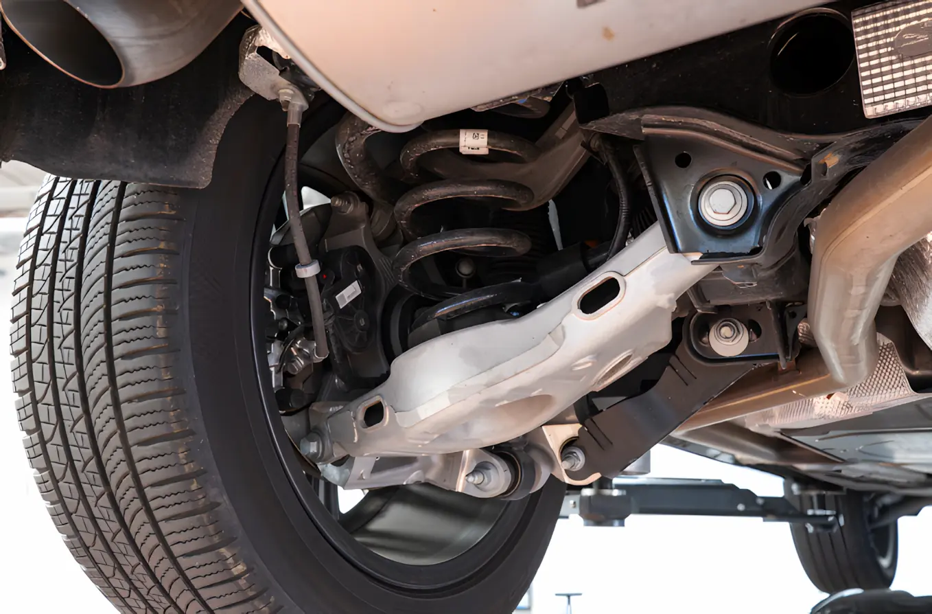 Text: Shpck and strut replacement, auto repair in New Braunfels, TX by Clark’s Auto Service. Image of a vehicle’s suspension system, including control arms and coil springs, highlighting improved ride comfort, handling, and long-term vehicle stability.