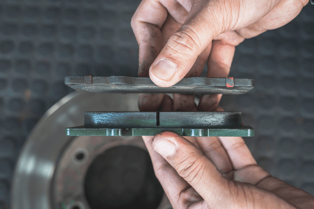 Brake pad replacement, auto repair in New Braunfels, TX at Clark’s Auto Service. Image of a technician comparing worn and new brake pads beside a brake rotor to help assess braking safety and maintenance needs.